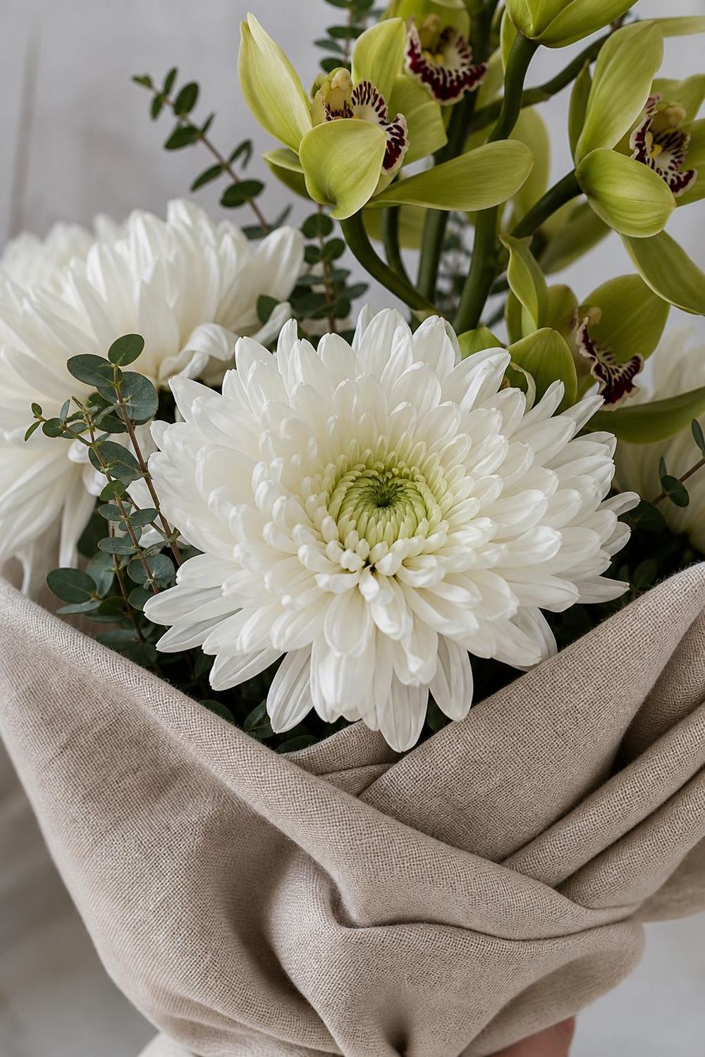 a bouquet of white Anastasia chrysanthemums and a green cymbidium spike on linen fabric, soft winter light