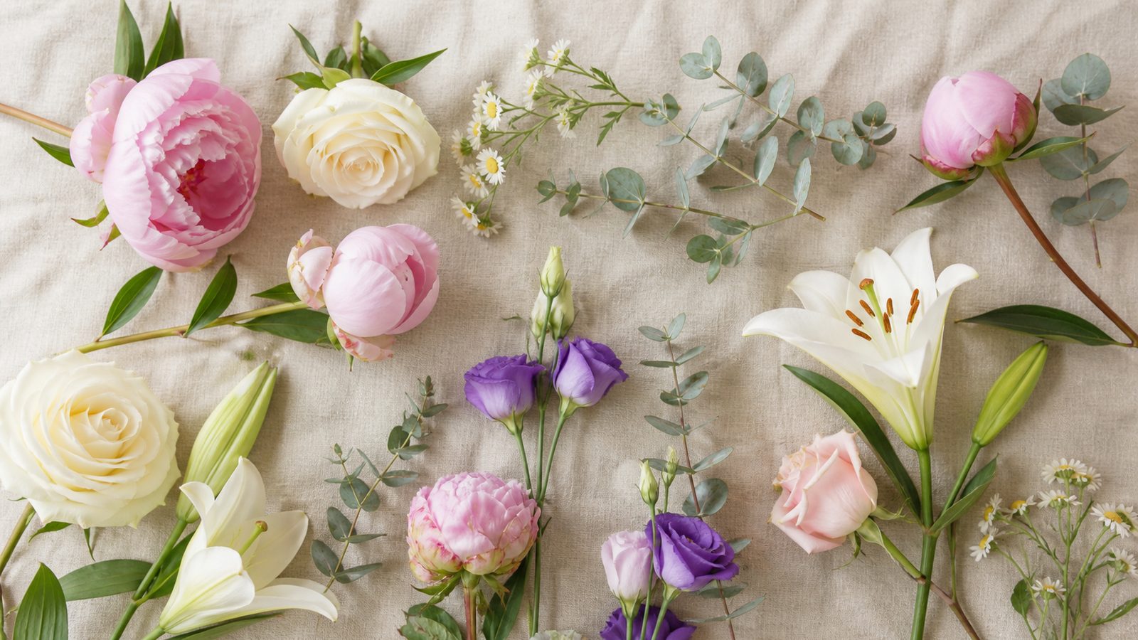 overhead flat-lay of assorted cut flowers — peonies, roses, lilies, daisies, lisianthus, eucalyptus — on natural linen, soft morning light, cream-pink palette
