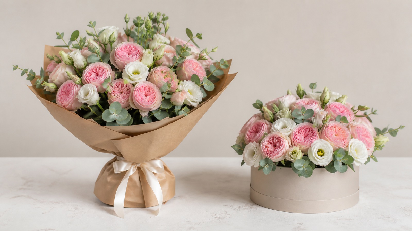 two arrangements side by side on a florist's white studio table — left, a classic French bouquet in kraft wrap with lush greenery; right, a compact hatbox with roses set in floral foam