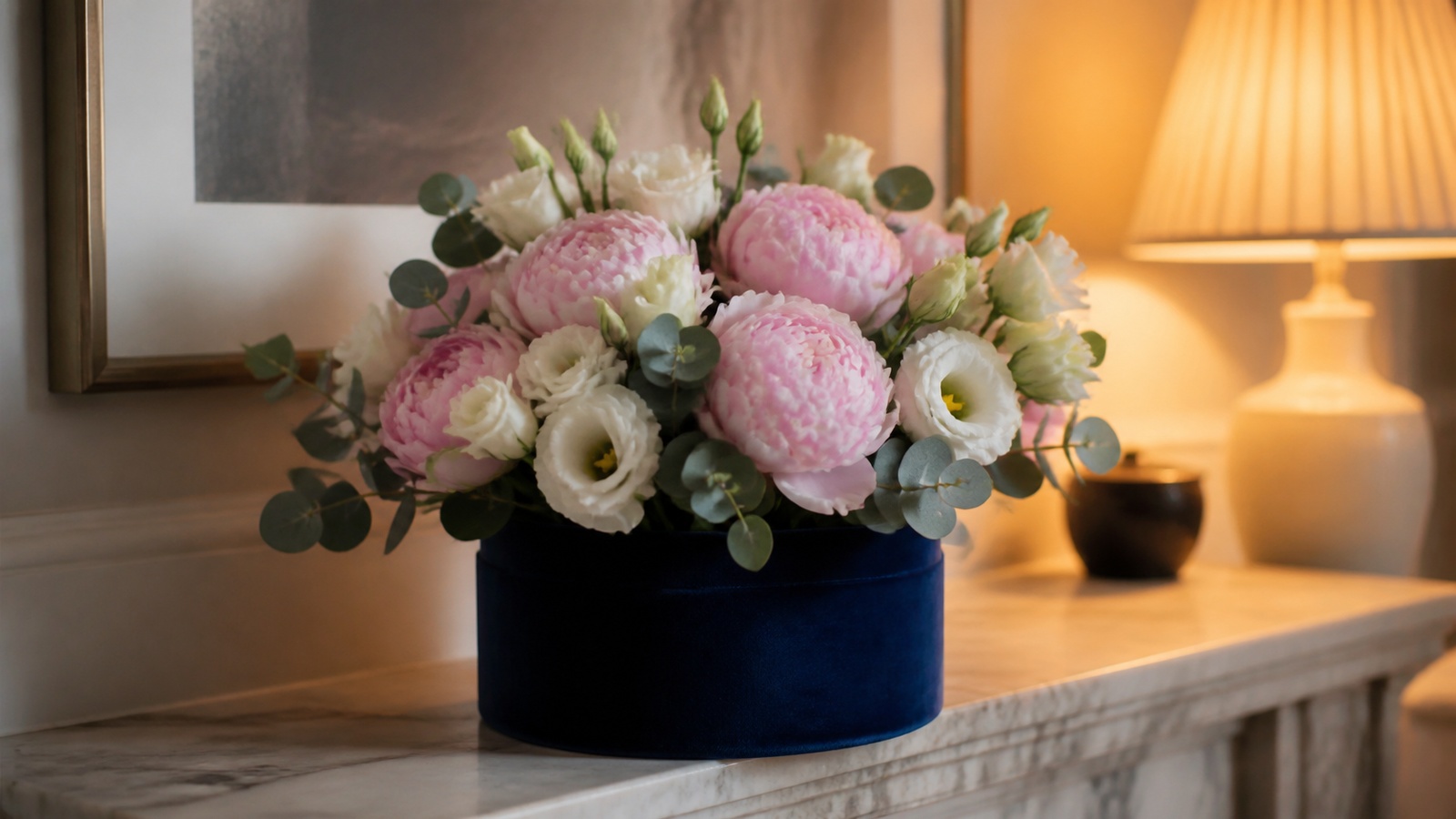 a navy blue velvet hatbox with pink peonies, white lisianthus and silver eucalyptus on an interior mantelpiece, lifestyle interior scene