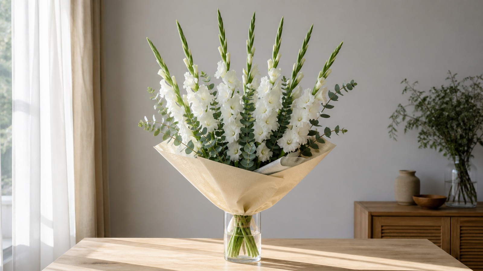 a mono-bouquet of 7 tall white gladiolus spikes with silver eucalyptus in kraft, on a wooden table, tall vertical composition
