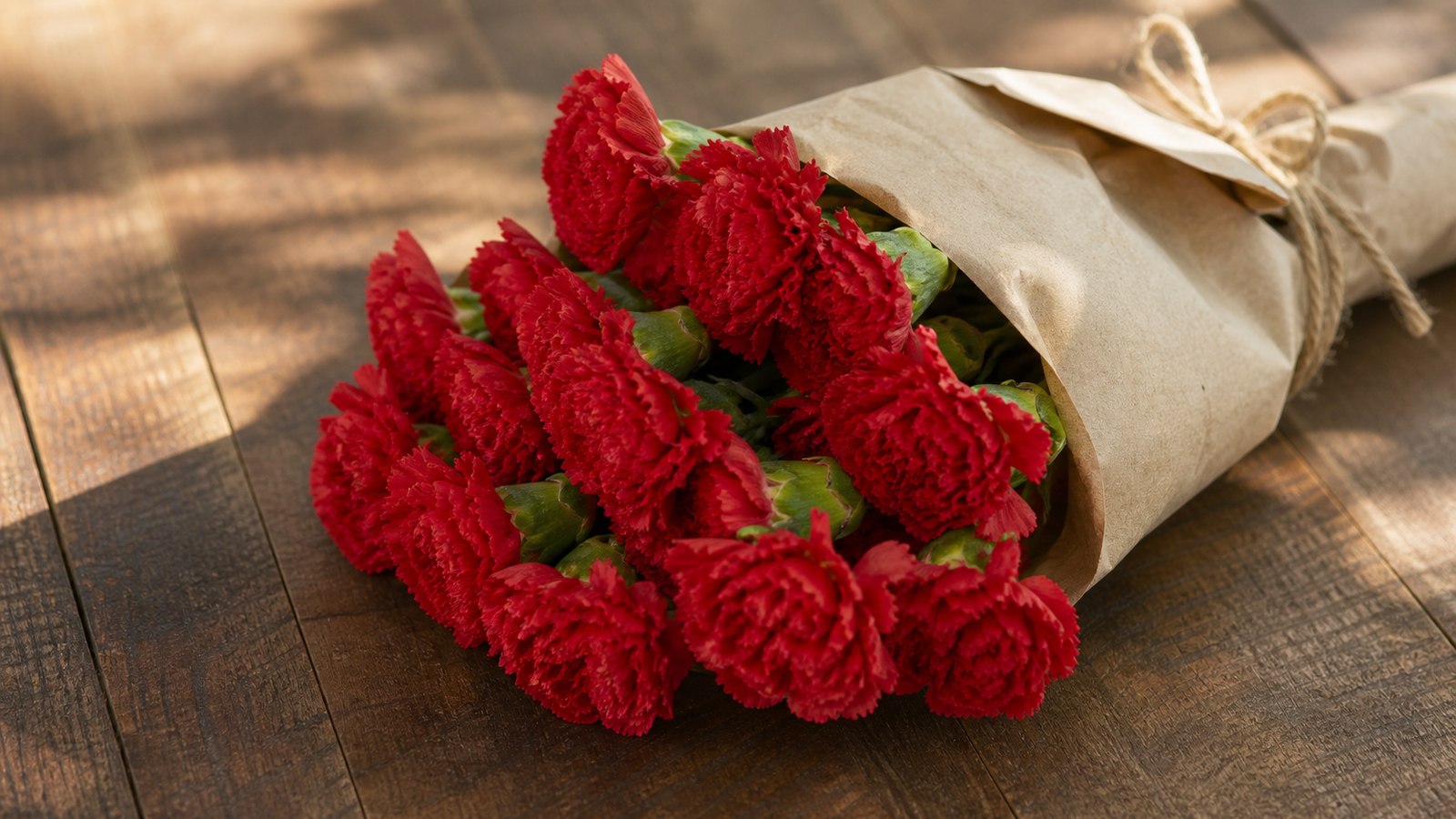 15 red Colombian carnations tied with jute in a natural brown paper wrap, on a rustic wooden table, warm afternoon light